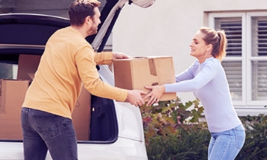 Parents moving boxes from car into their house